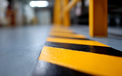 Floor-level perspective highlights a bold yellow and black safety stripe on a grey concrete surface. The mood is industrial, with a sense of caution and work. Use for safety, factory, or maintenance contexts
